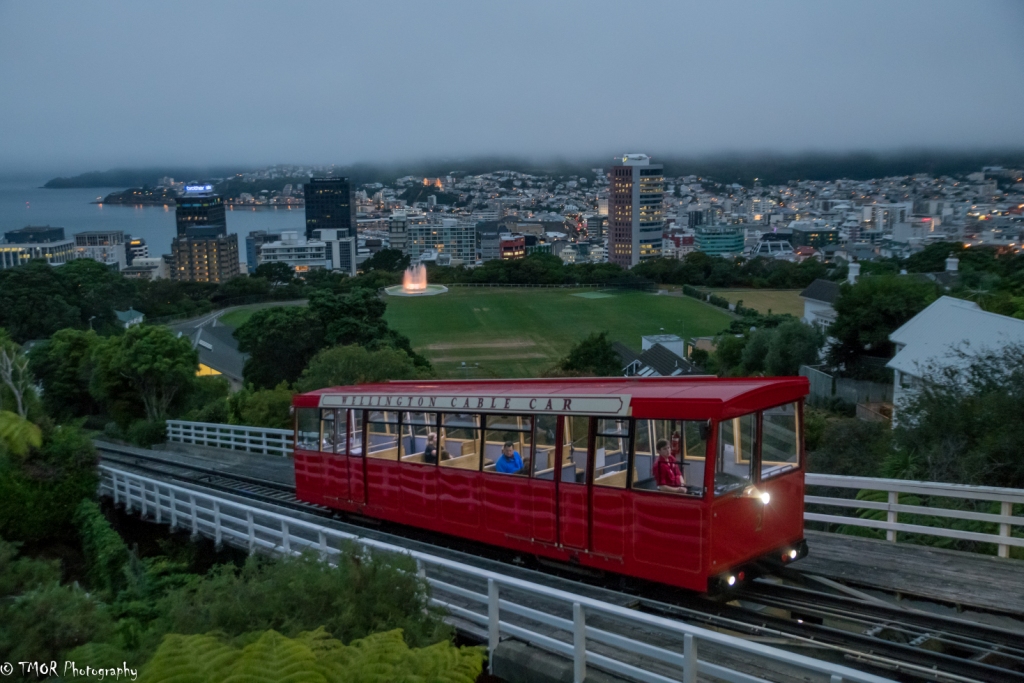 Red trolly on road with city in the background